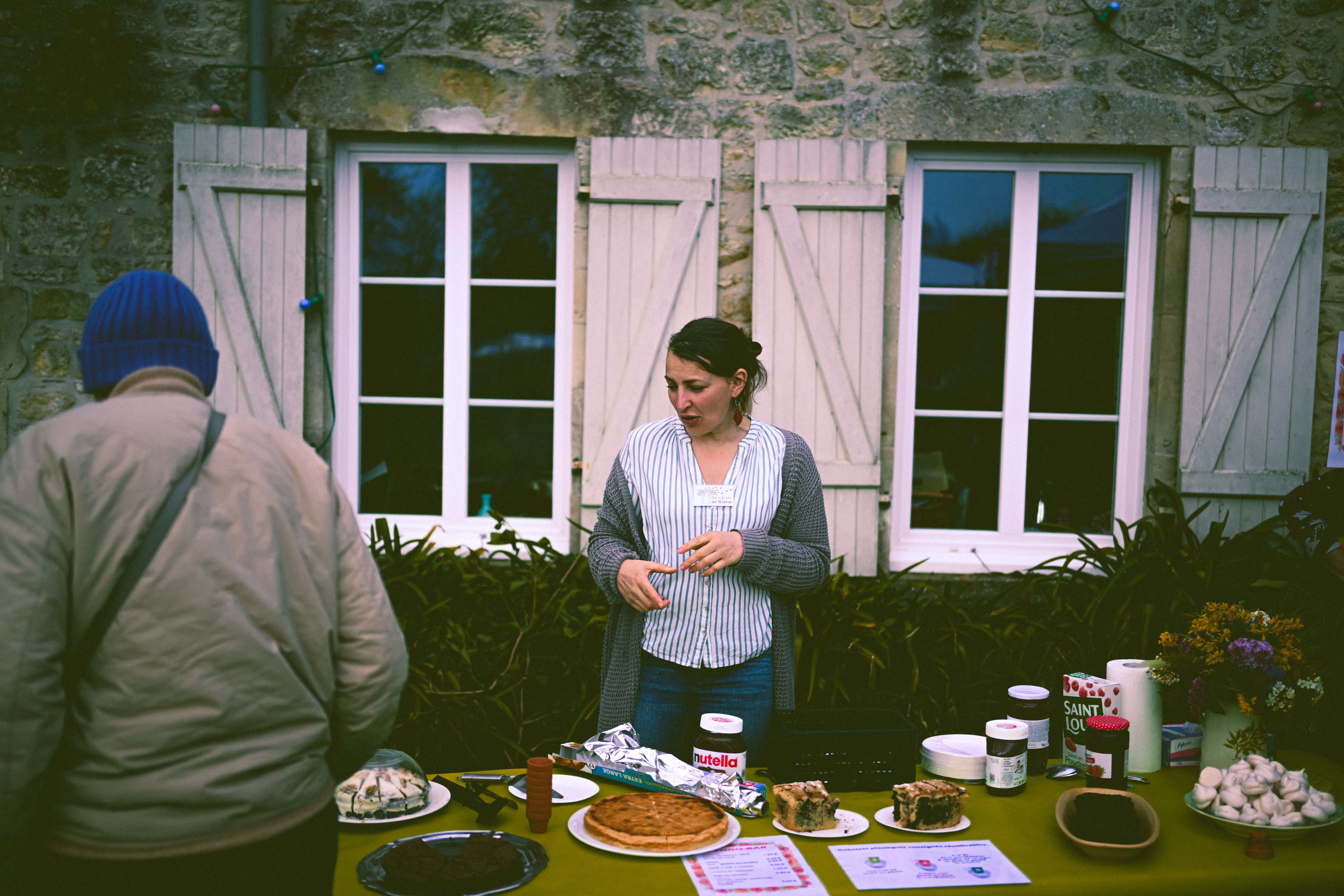 Woman arranging homemade cakes and pastries at a market stall, suggesting a creative bake-sale menu.